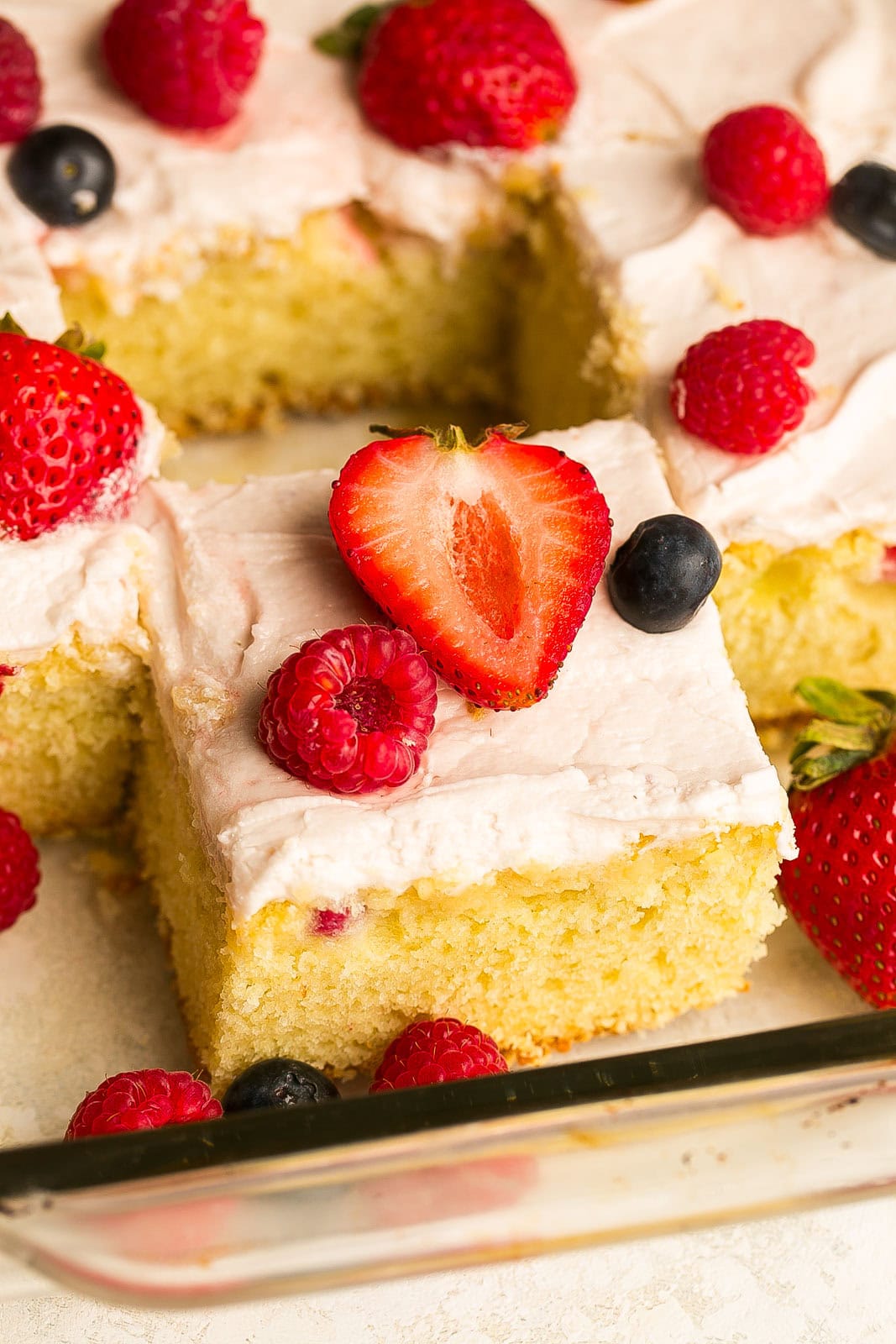 Cut Berry Yogurt Cake in sheet pan with frosting and berries on top.