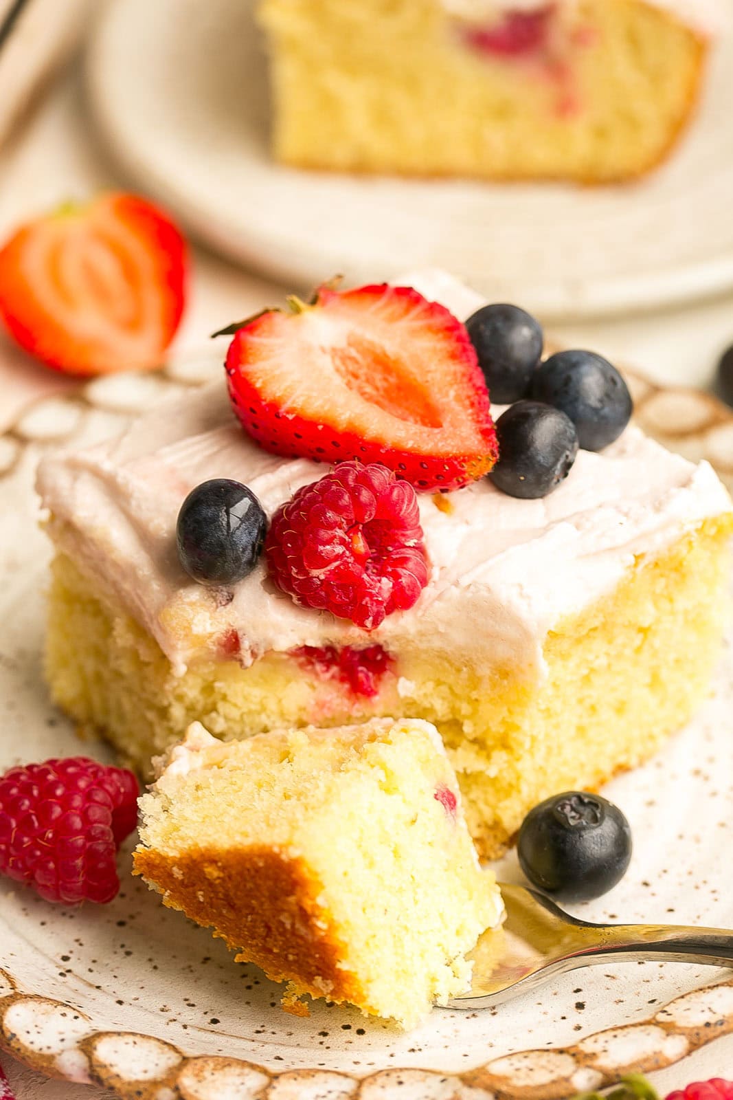 Fresh berry yogurt cake with a tender crumb, creamy frosting, and a topping of mixed summer berries.