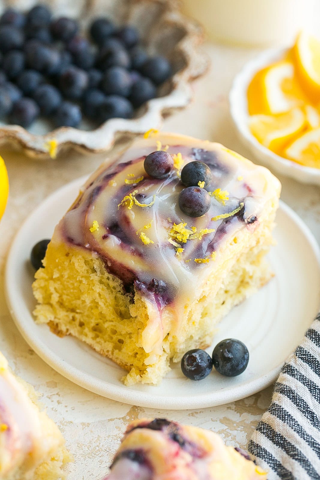 Blueberry lemon sweet roll served on a white plate with lemon cream cheese frosting.