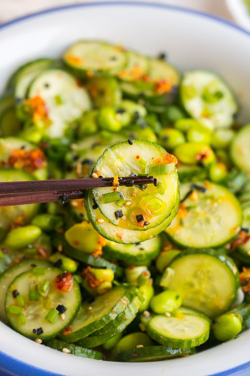 Close up of chopsticks holding cucumber with sesame ginger dressing.