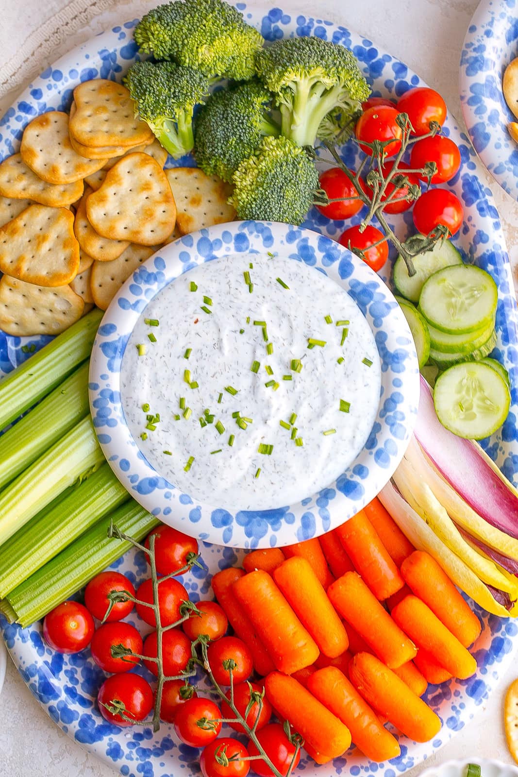 Creamy Greek yogurt ranch dip in a bowl garnished with fresh chives and served with carrots, cucumbers, celery, broccoli, and cherry tomatoes, and crackers.
