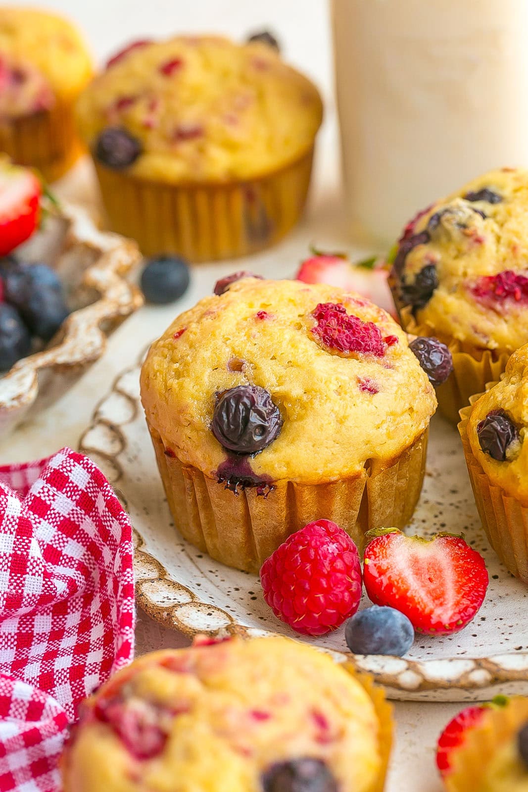 A perfect bakery-style muffin on a plate with strawberries, blueberries and raspberries.