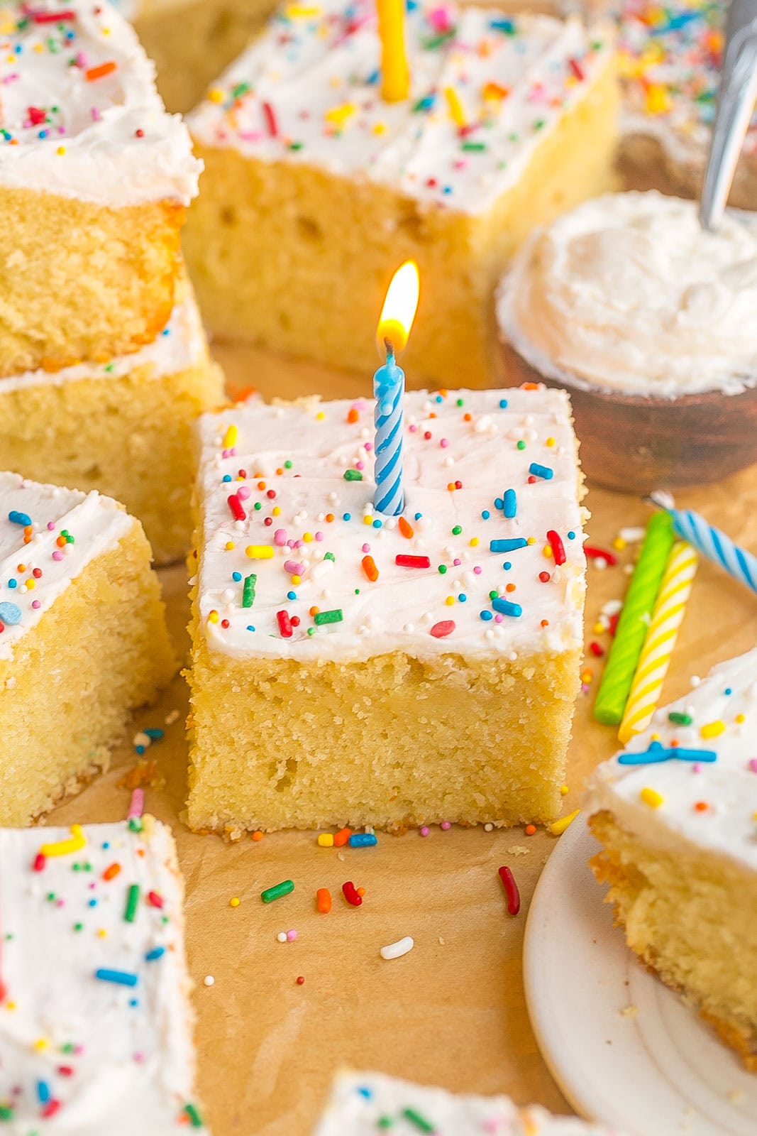 Classic Vanilla Sheet Cake recipe with fluffy vanilla buttercream frosting, sliced and ready to enjoy with a lite blue candle.