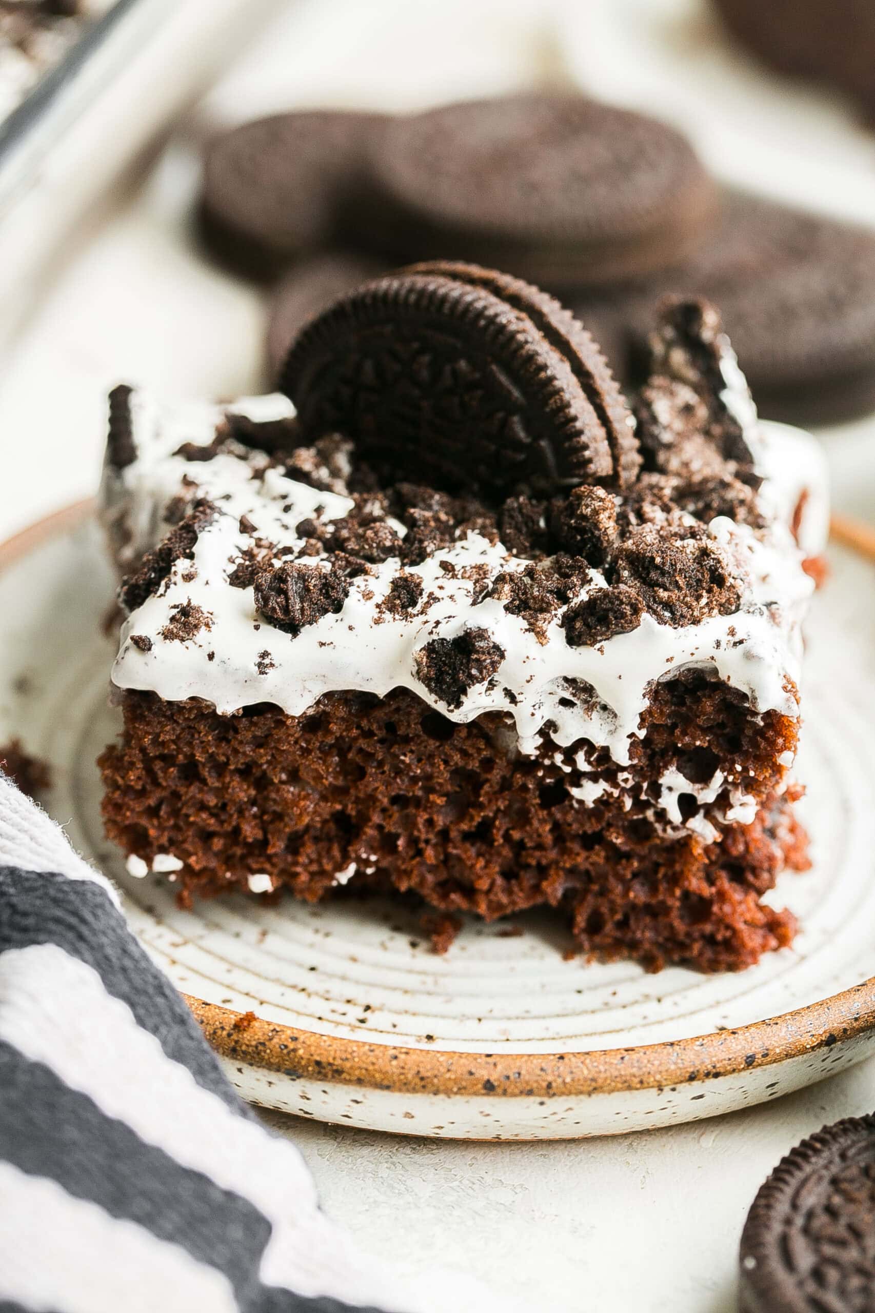 Close-up of a slice of Oreo Poke Cake featuring chocolate cake, cookies and cream pudding, whipped topping, and crushed Oreo cookies.