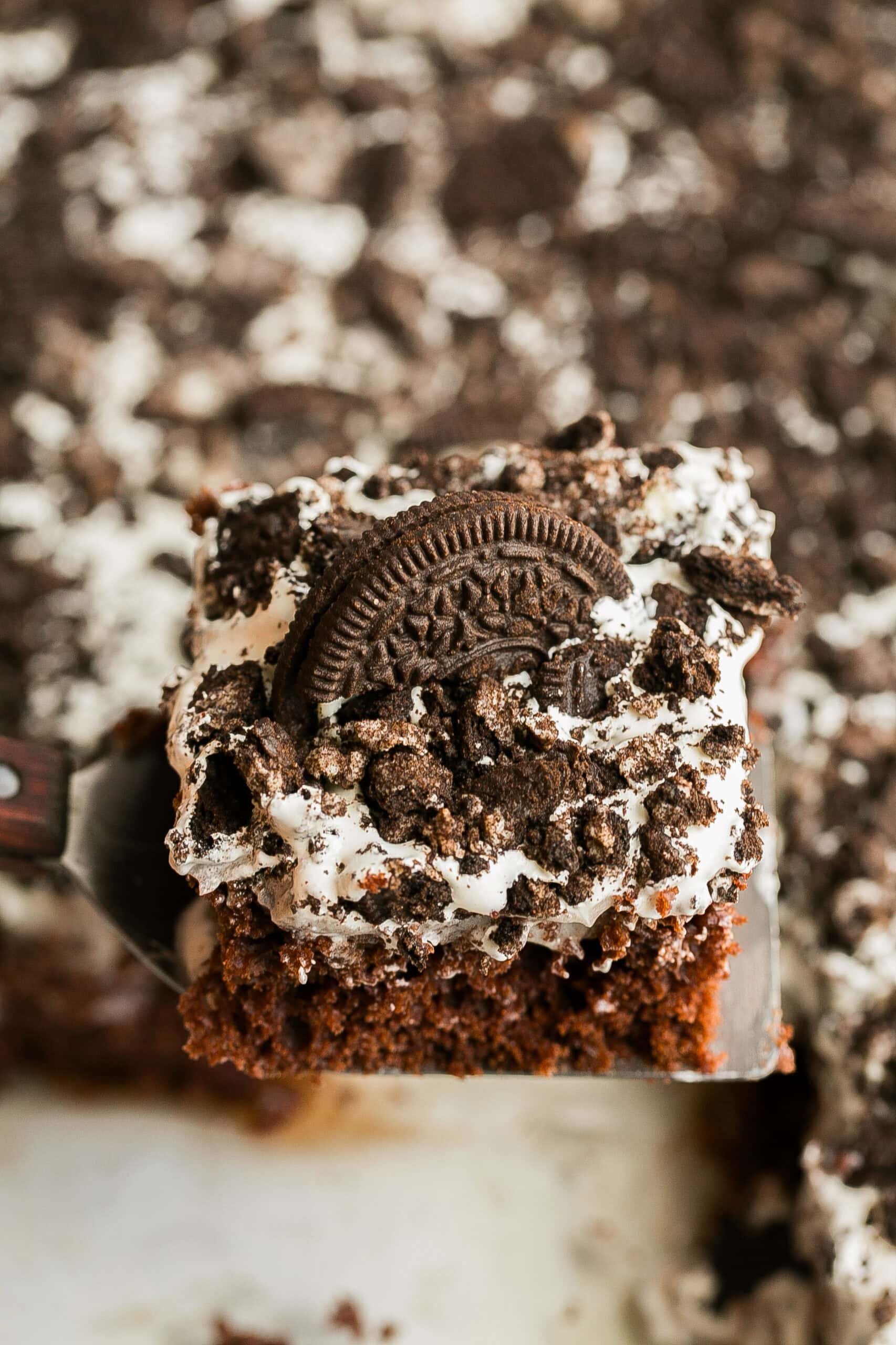 Chocolate Oreo Poke Cake decorated with whipped topping, Oreo cookie crumbs, mini Oreos, and chocolate drizzle.